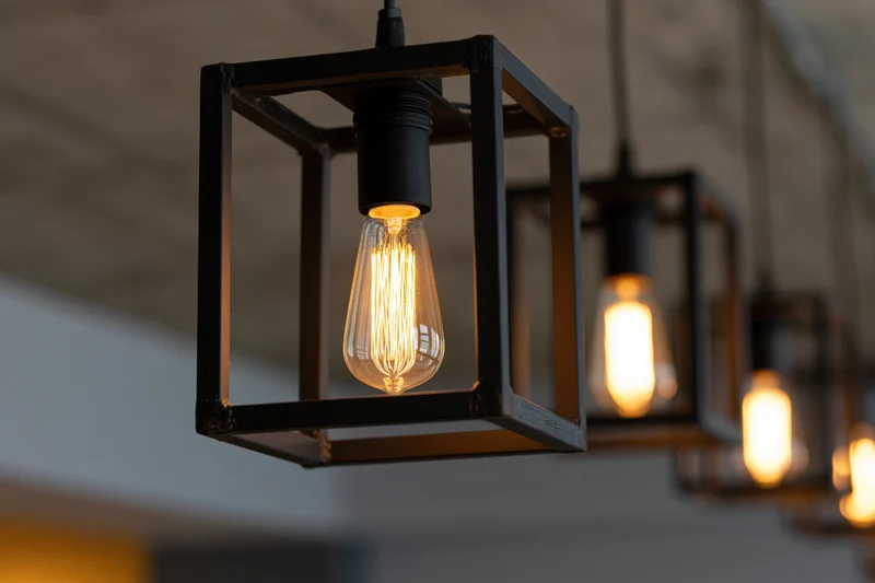 Edison filament bulbs suspended inside open black metal cubes in a row along a ceiling