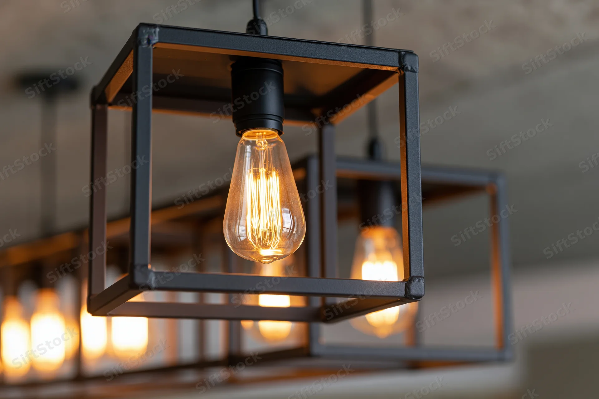Edison filament bulbs suspended inside open black metal cube frames hanging from ceiling in interior space