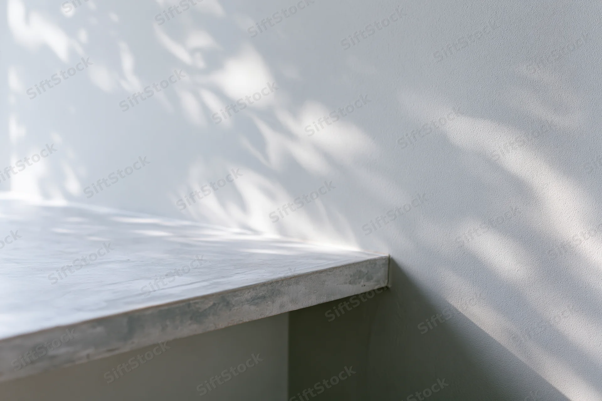 Concrete surface with dappled shadows from foliage against a plain grey wall