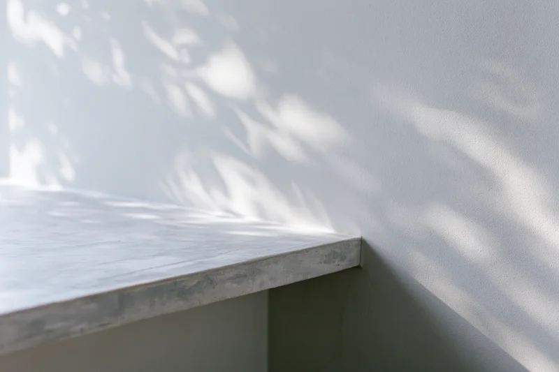 Concrete surface with dappled shadows from foliage against a plain grey wall