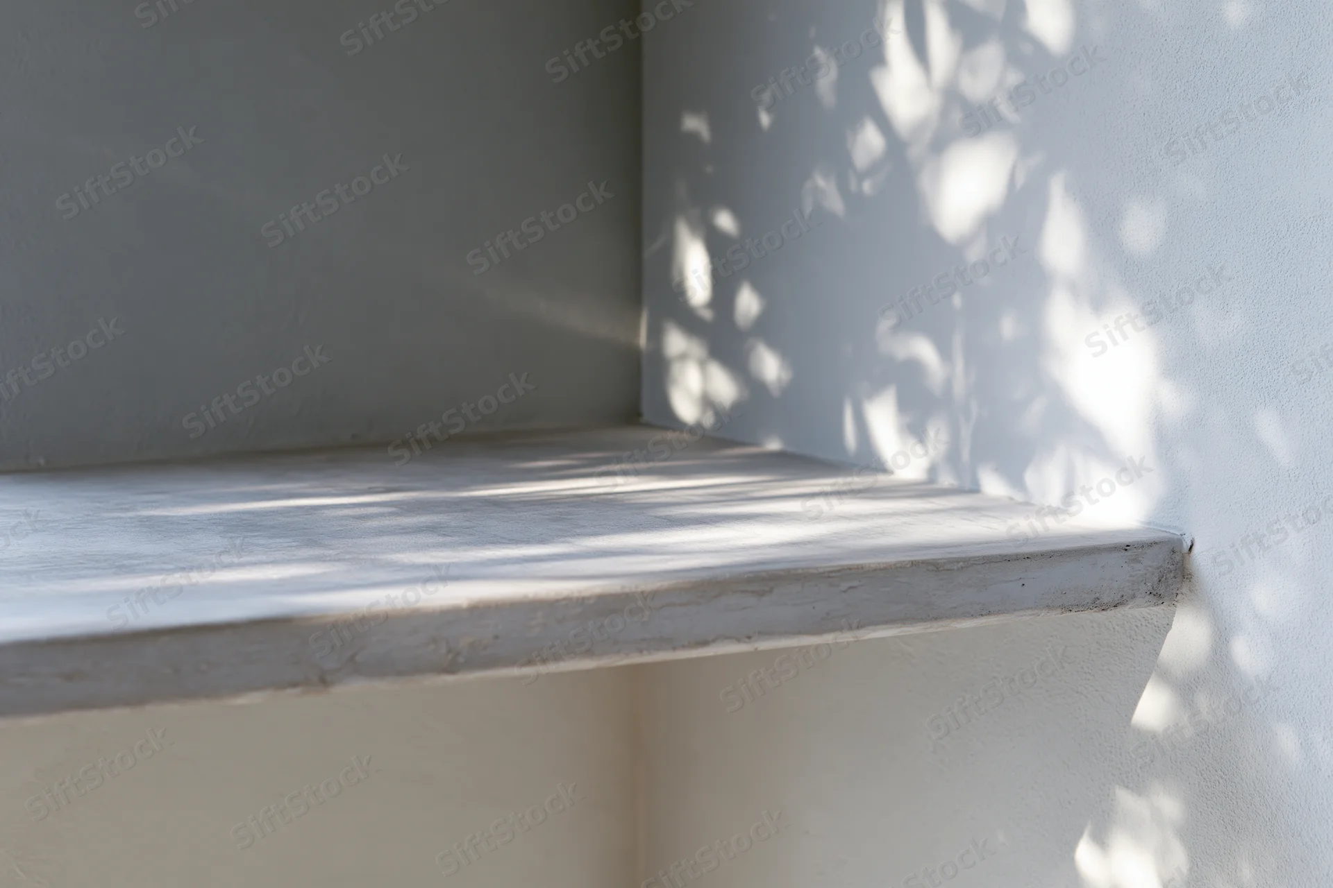 Concrete shelf in corner of gray wall with dappled sunlight and leaf shadows