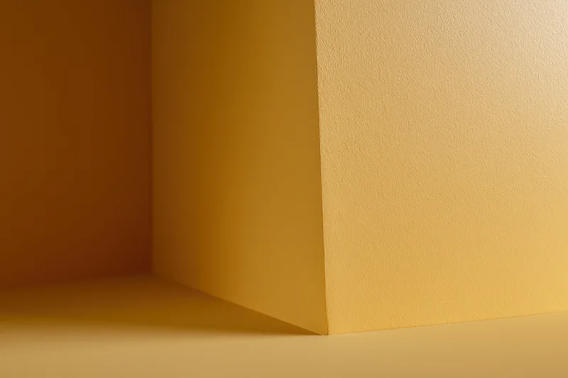 Empty corner of a room with golden yellow painted walls and floor, showing shadow and light gradient