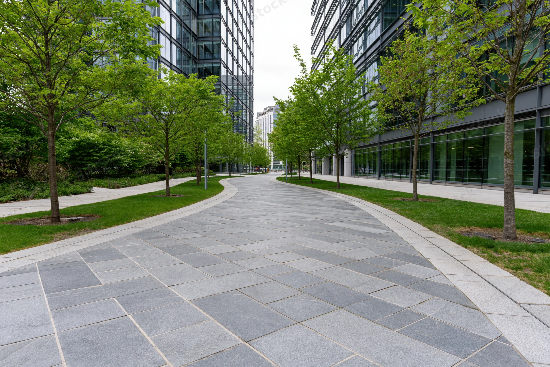 Curved stone-paved walkway winding between modern glass office buildings in an urban plaza setting