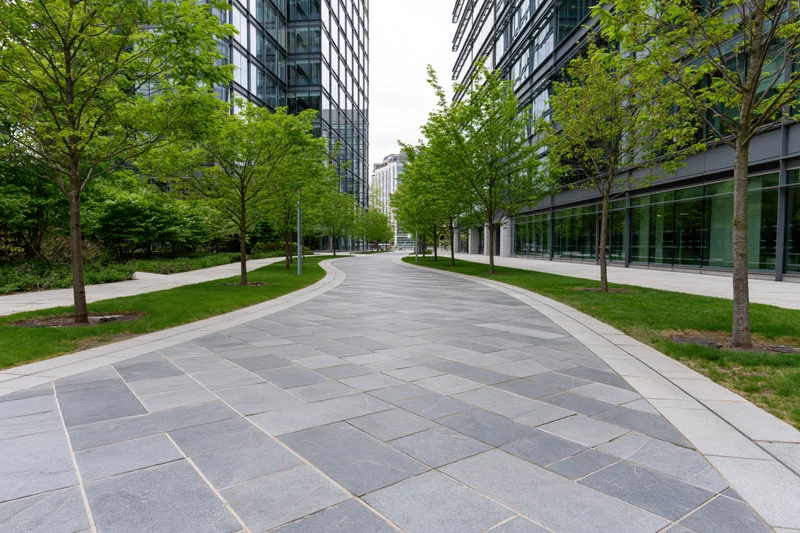 Curved stone-paved walkway winding between modern glass office buildings in an urban plaza setting