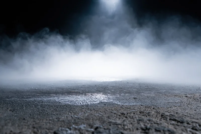 Dense white smoke rising from a dark wet concrete floor at night