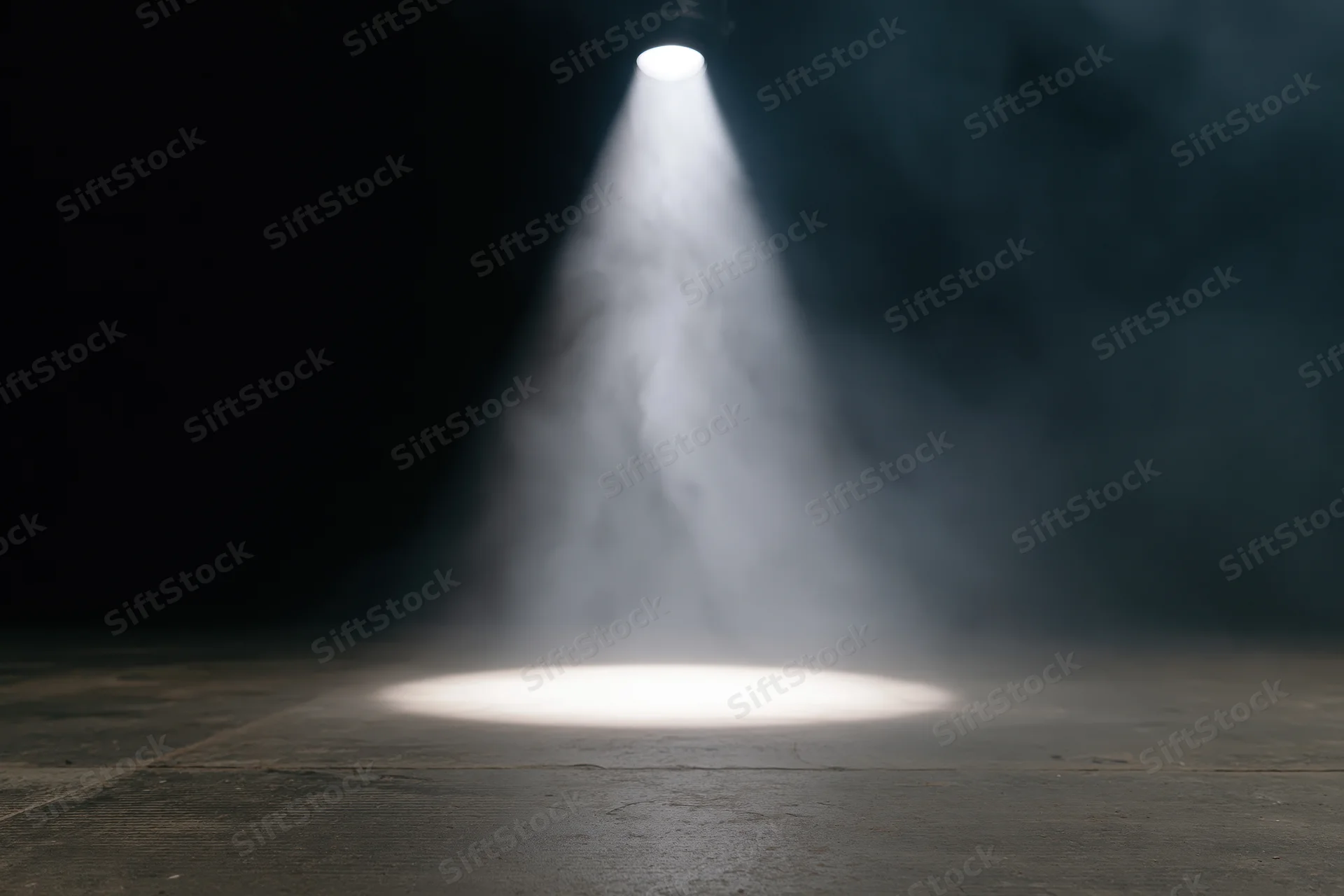 Single overhead spotlight beam on empty dark stage floor