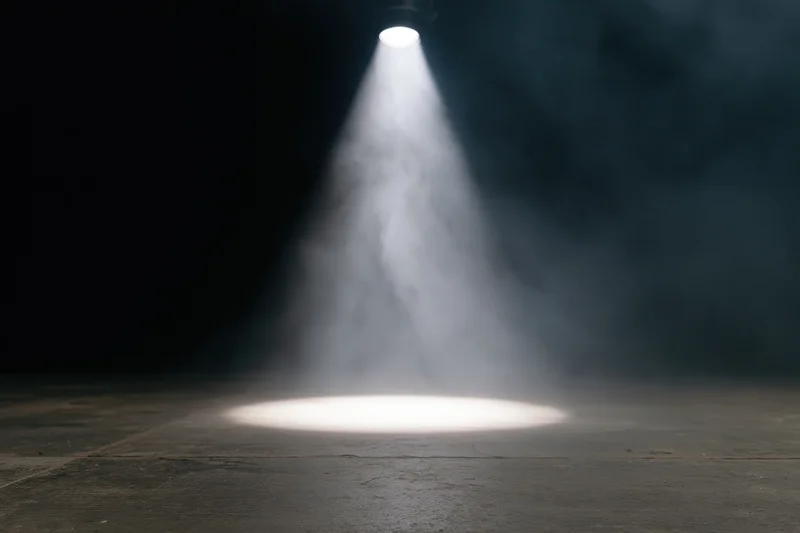 Single overhead spotlight beam on empty dark stage floor