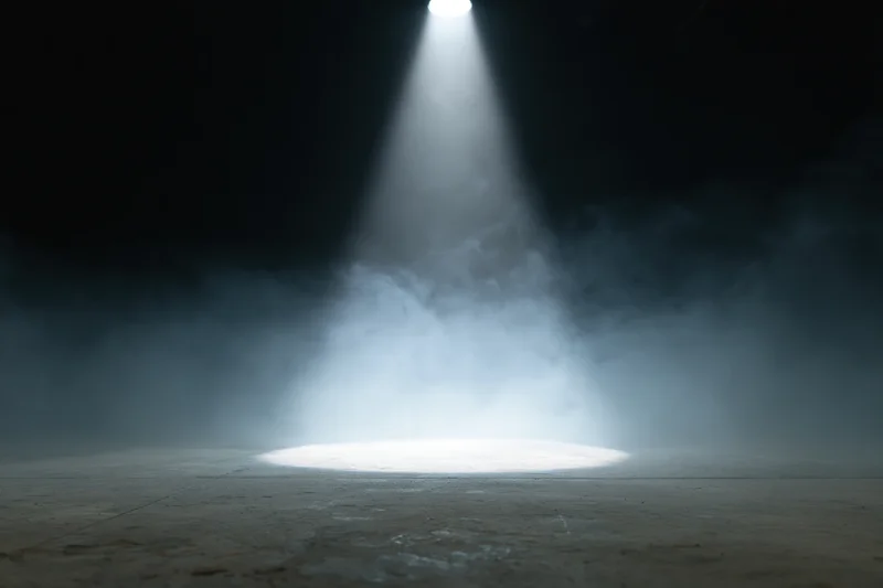 Single spotlight beam illuminating empty stage floor in dark theater