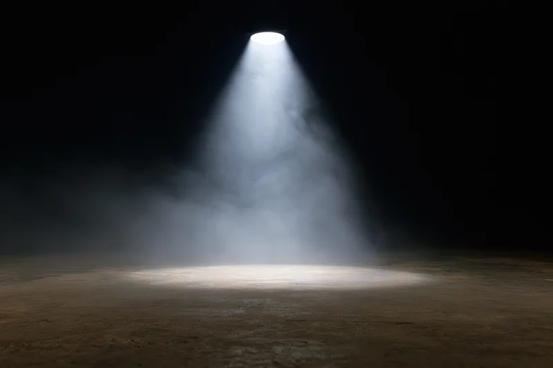 Single overhead spotlight beam illuminating empty dark stage floor
