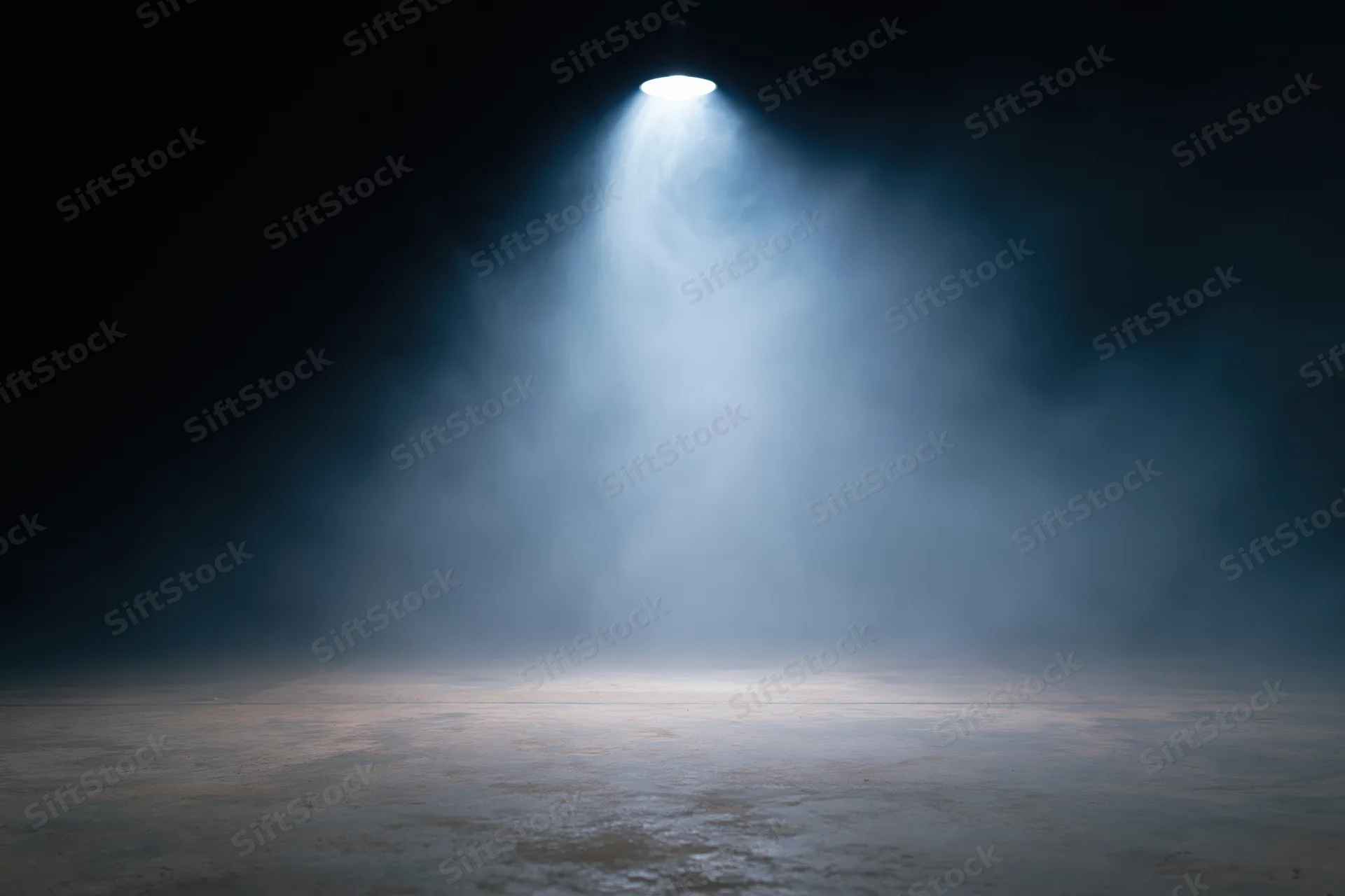 Single overhead spotlight illuminating an empty dark stage with fog and textured floor