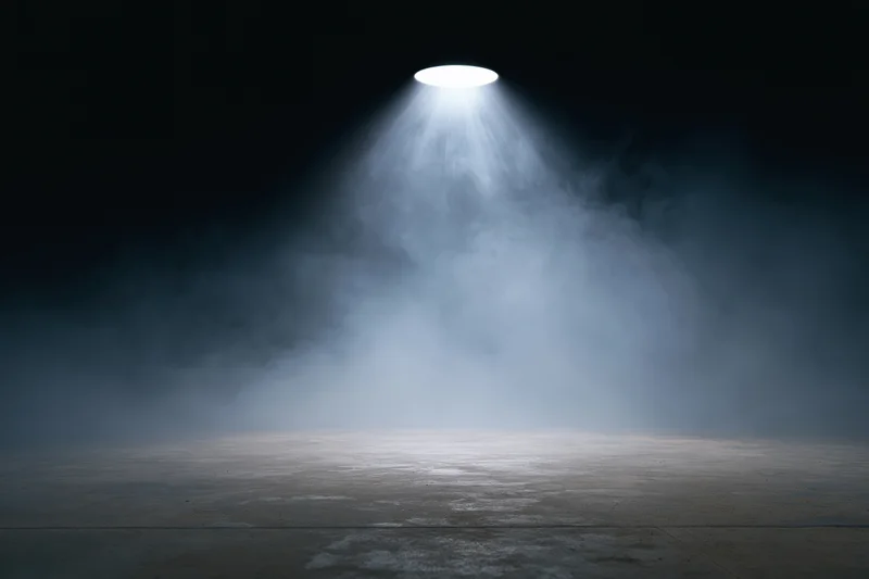 Empty dark stage illuminated by a single overhead spotlight with fog on the floor