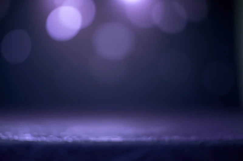 Dark studio backdrop with blurred purple bokeh lights and a faint surface ledge at bottom