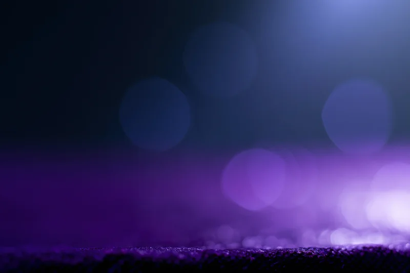 Dark studio backdrop with blurred purple and blue bokeh lights above a textured surface ledge