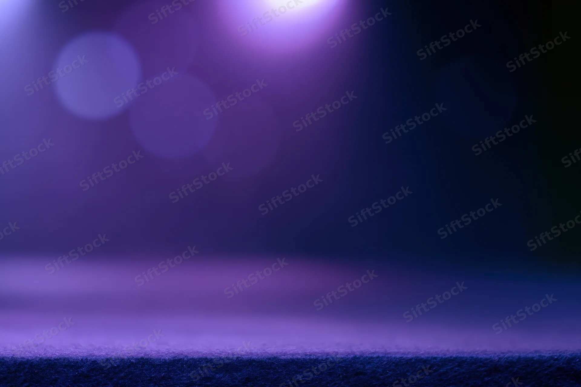 Dark studio backdrop with purple and blue bokeh lighting and a faint surface ledge at the bottom