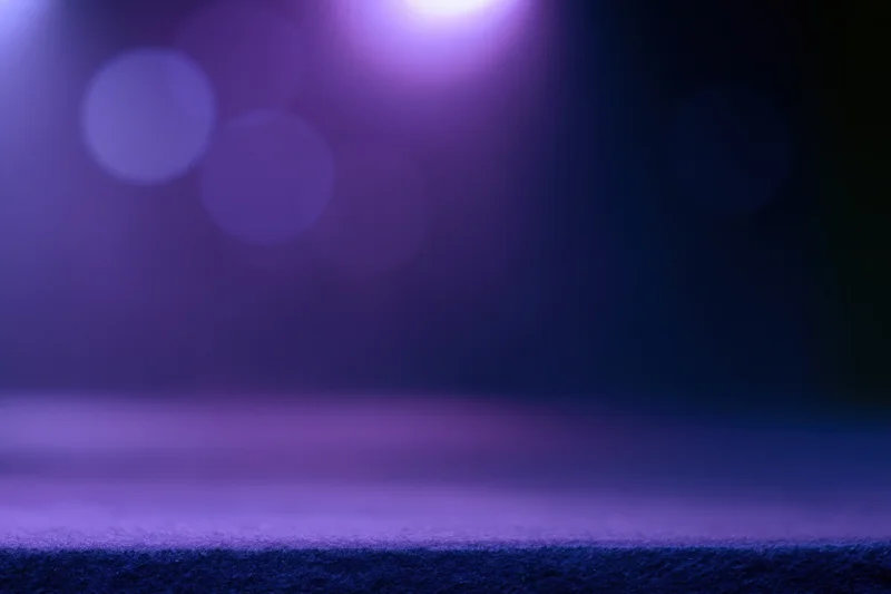 Dark studio backdrop with purple and blue bokeh lighting and a faint surface ledge at the bottom