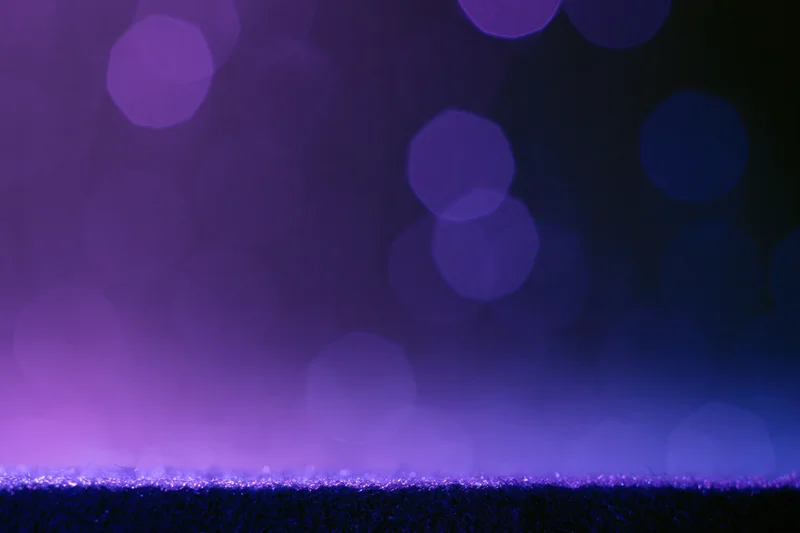 Dark studio backdrop with a glowing purple ledge and blurred bokeh lights above