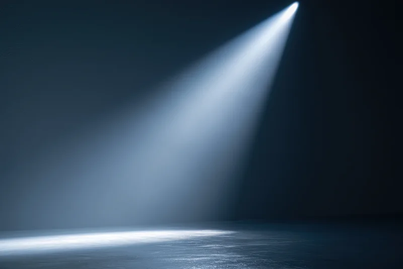Single spotlight beam illuminating empty dark studio floor with reflection and haze