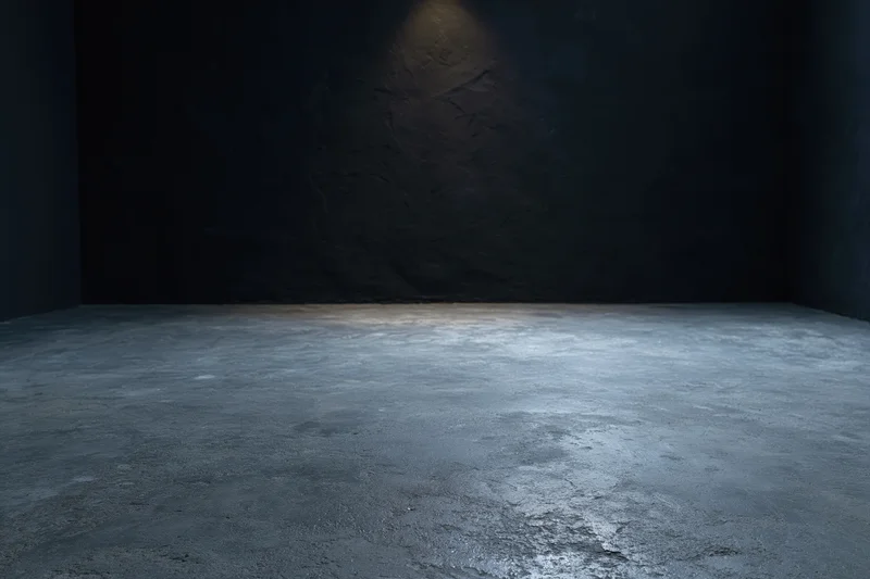 Dark empty studio interior with rough concrete floor and spotlighted wall