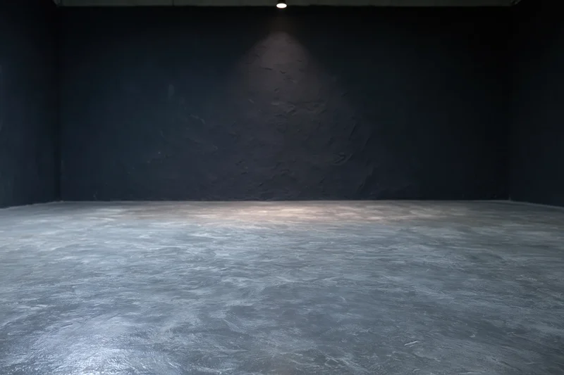 Empty dark studio interior with rough concrete floor and spotlight on textured wall