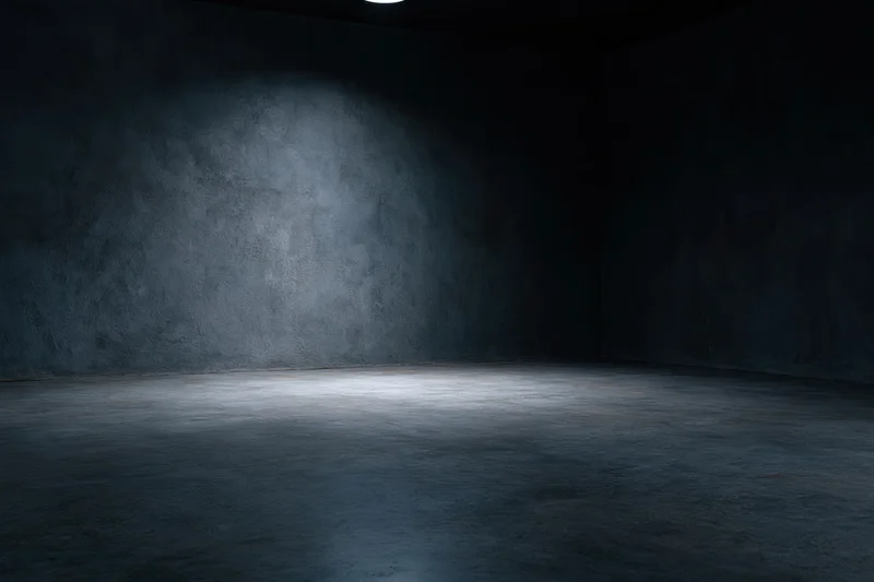 Empty dark studio room with concrete textured walls and floor lit by a single spotlight creating a moody atmosphere with copyspace