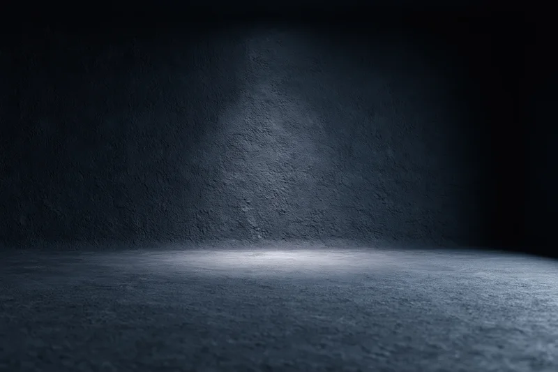Empty dark studio room with concrete textured wall and floor lit by spotlight