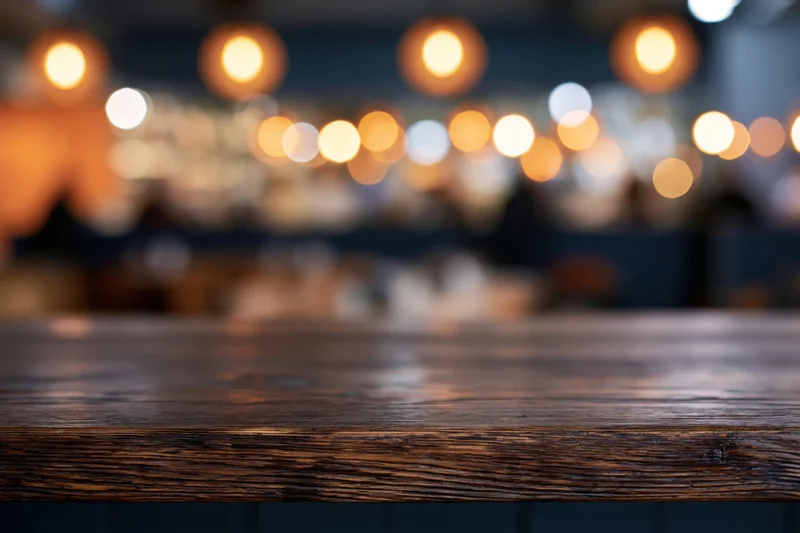 Dark wooden bar counter in sharp focus with blurred lights in background
