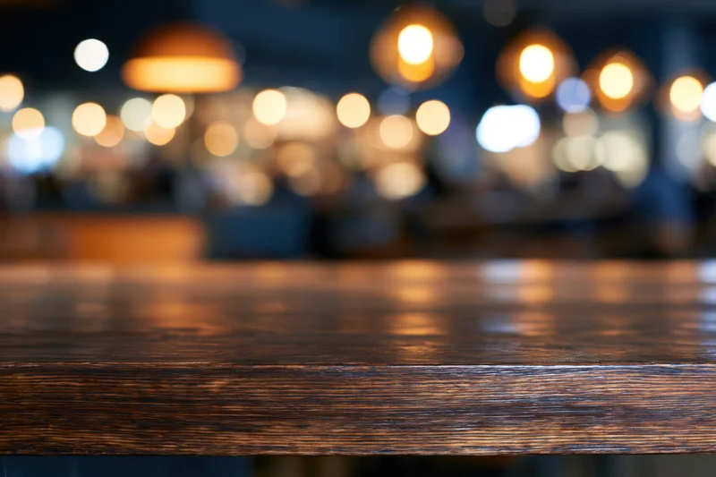 Dark wooden bar counter in sharp focus with blurred lights in background