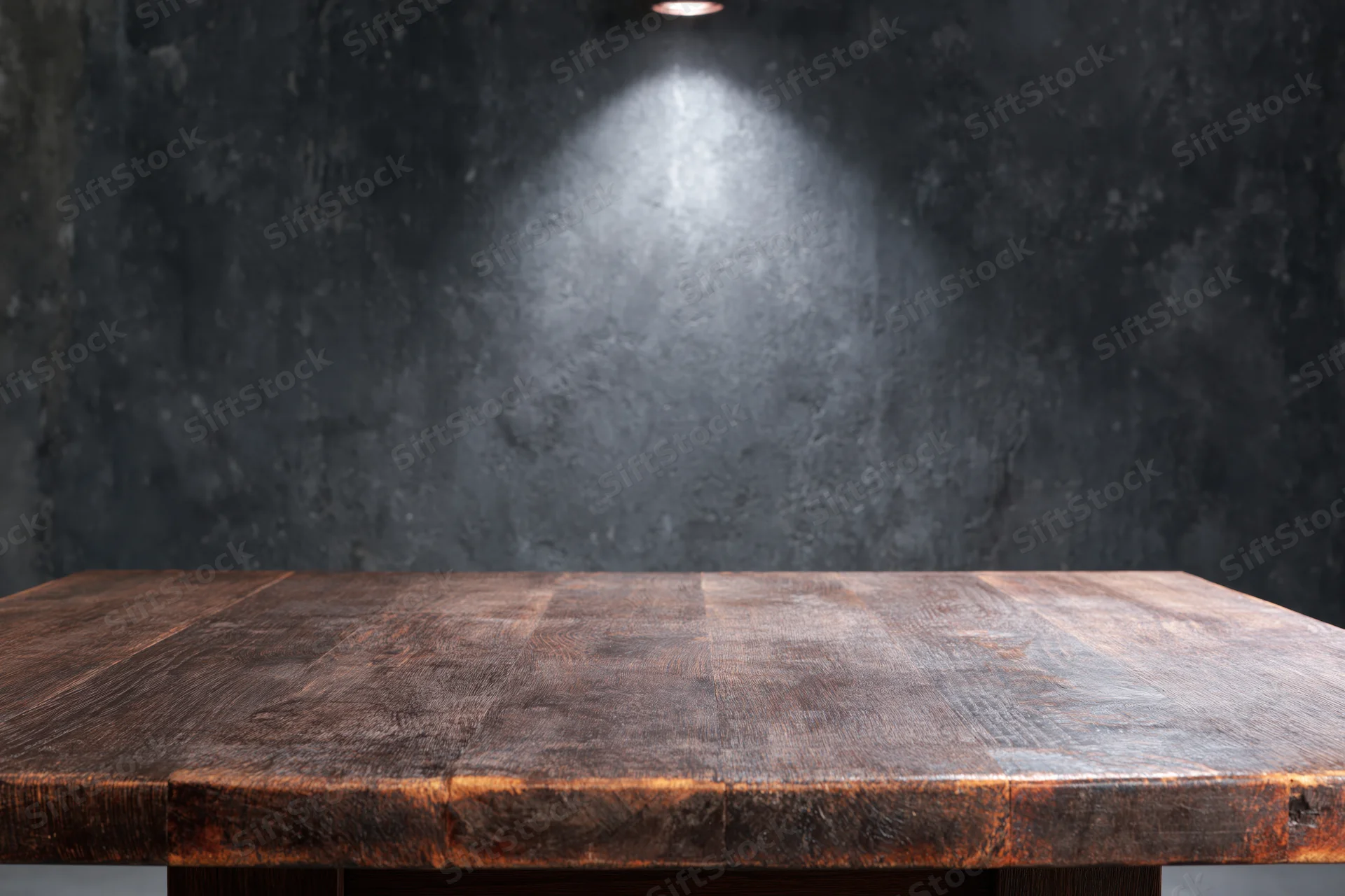 Dark rustic wooden tabletop in foreground with spotlight on textured concrete wall behind