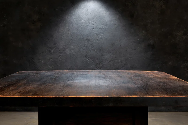 Dark wooden table surface with spotlight against textured black wall, empty and rustic, interior setting