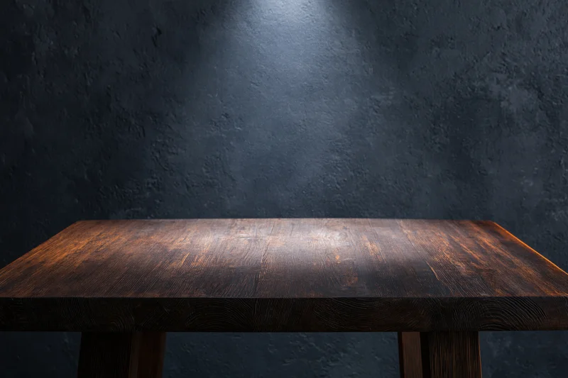 Empty dark wooden tabletop surface in front of textured dark wall with spotlight and copyspace