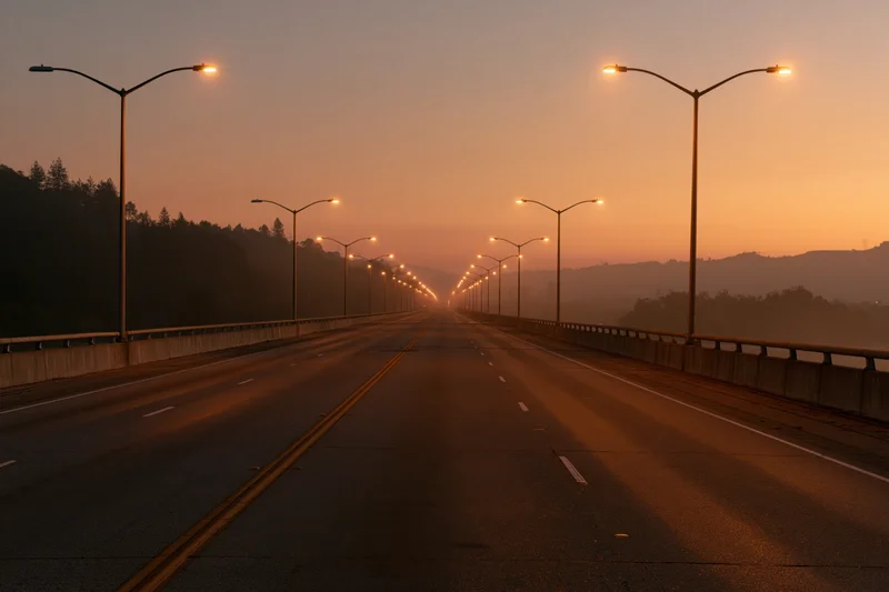 Empty four-lane highway stretching toward the horizon on a bridge at sunset with streetlights lining both sides