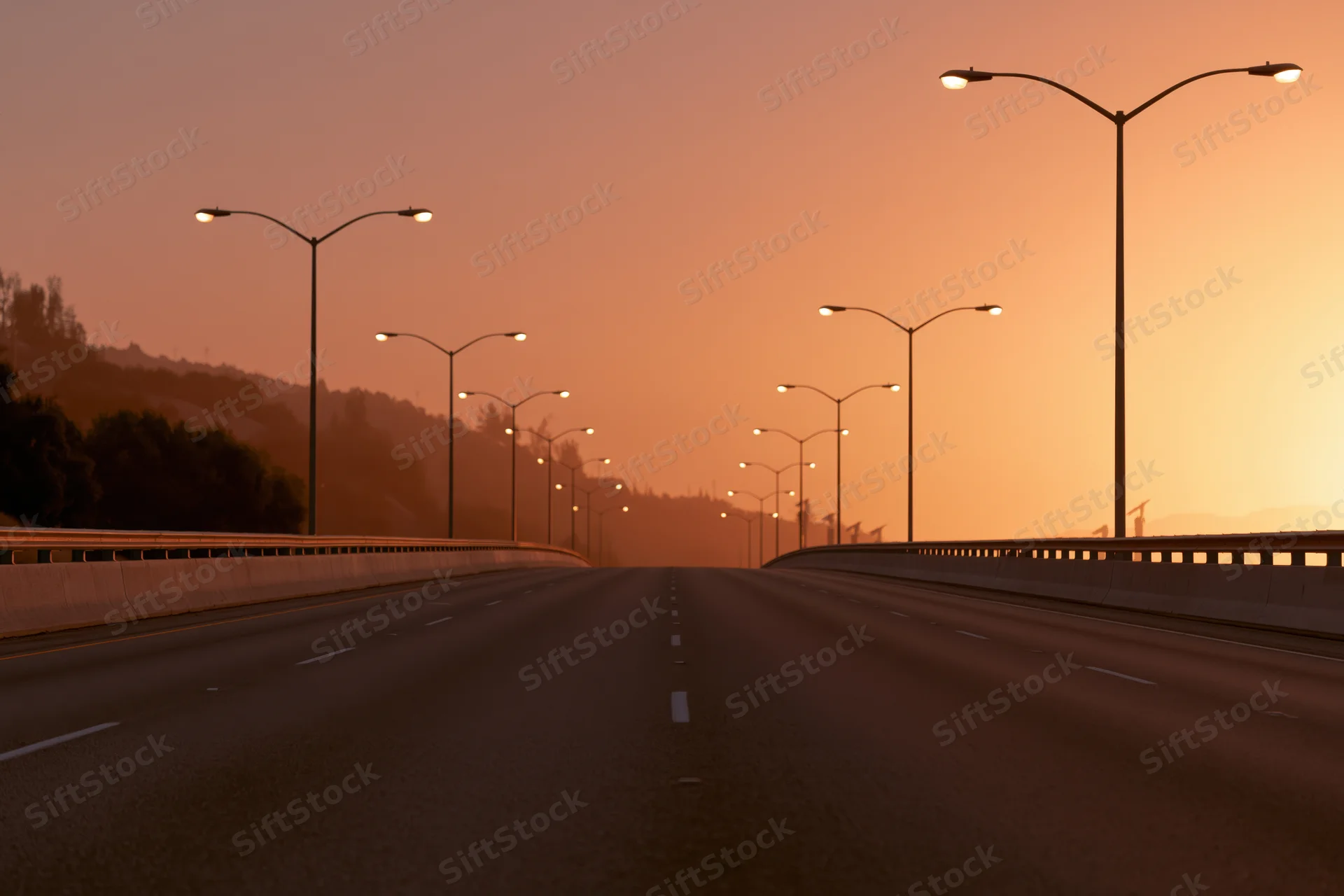 Empty four-lane highway stretching toward the horizon lined with streetlights at sunset