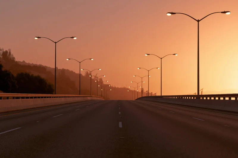 Empty four-lane highway stretching toward the horizon lined with streetlights at sunset
