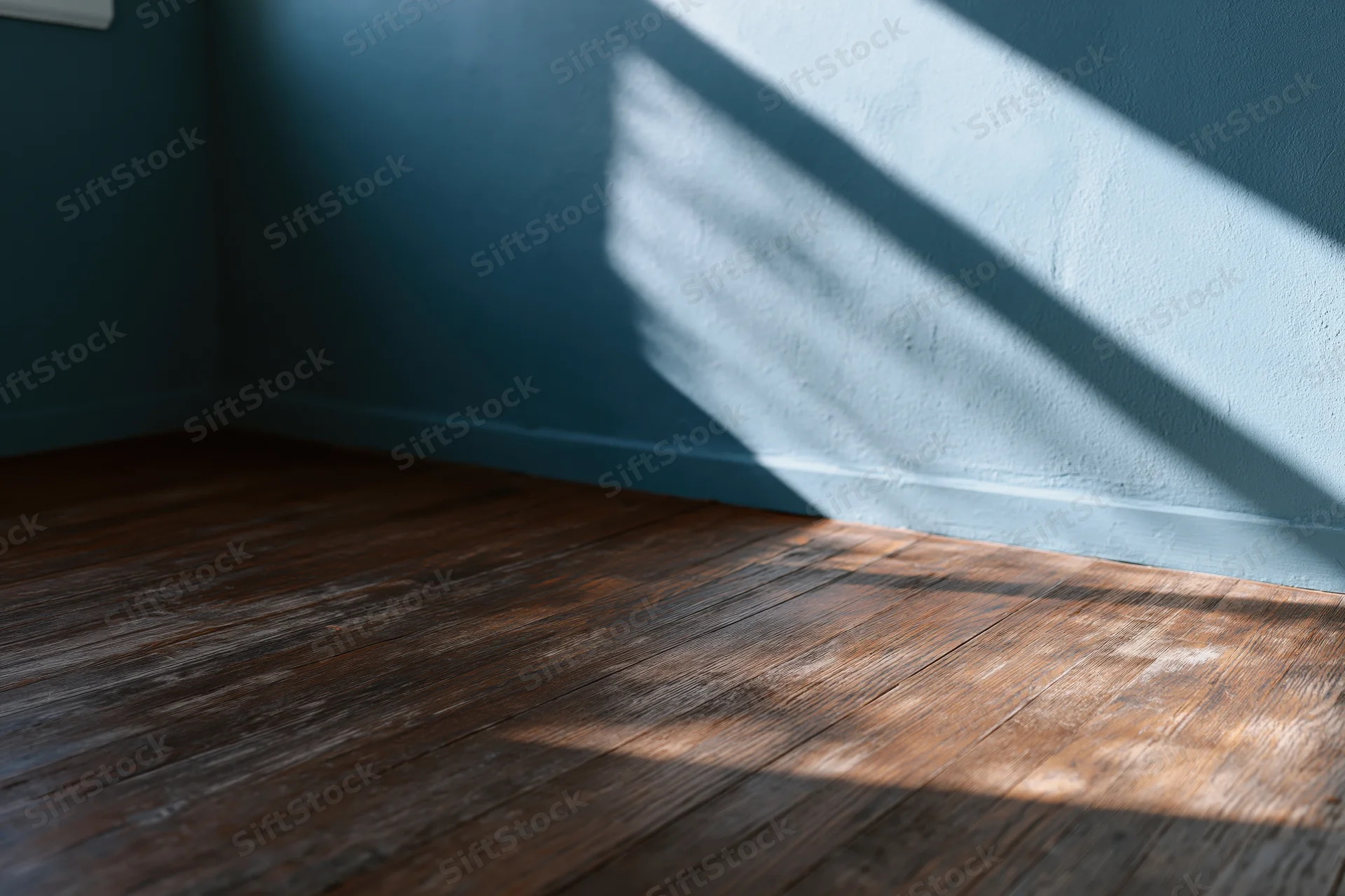 Empty room corner with dark teal-grey painted wall and worn wooden floor lit by diagonal sunlight casting striped shadows