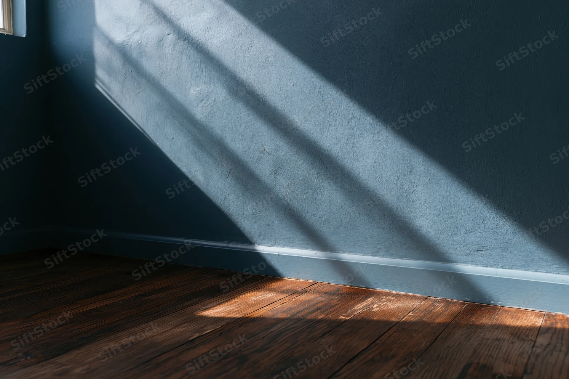 Sunlight casting diagonal shadows on dark teal wall and wooden floor in empty room corner