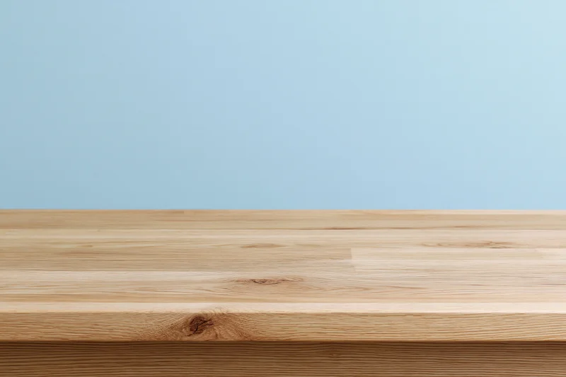 Empty light oak wooden tabletop surface against a plain blue background with copyspace for product display
