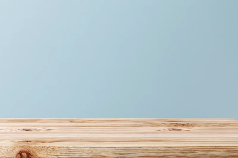 Light oak wooden tabletop surface with visible grain and knots against a plain blue background