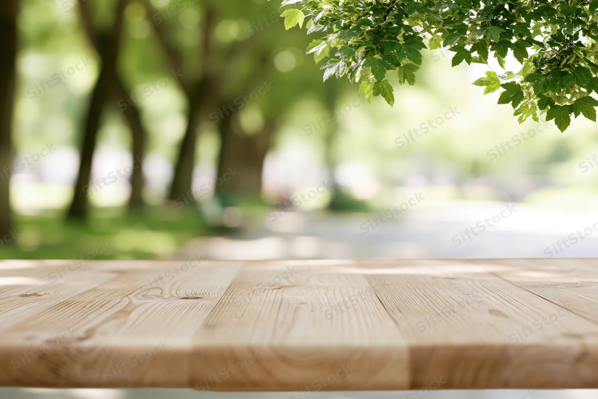 Empty light pine wood table surface in a park with green trees and foliage in the background