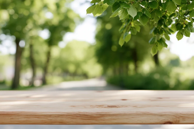 Empty light pine wood table surface in a park with green foliage and blurred background