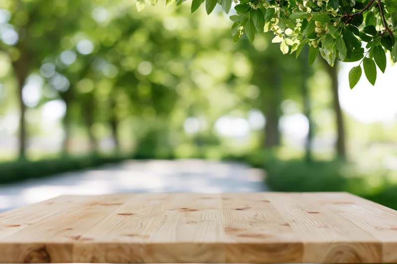 Empty pine wood table surface in a sunlit garden with blurred green foliage and a pathway in the background