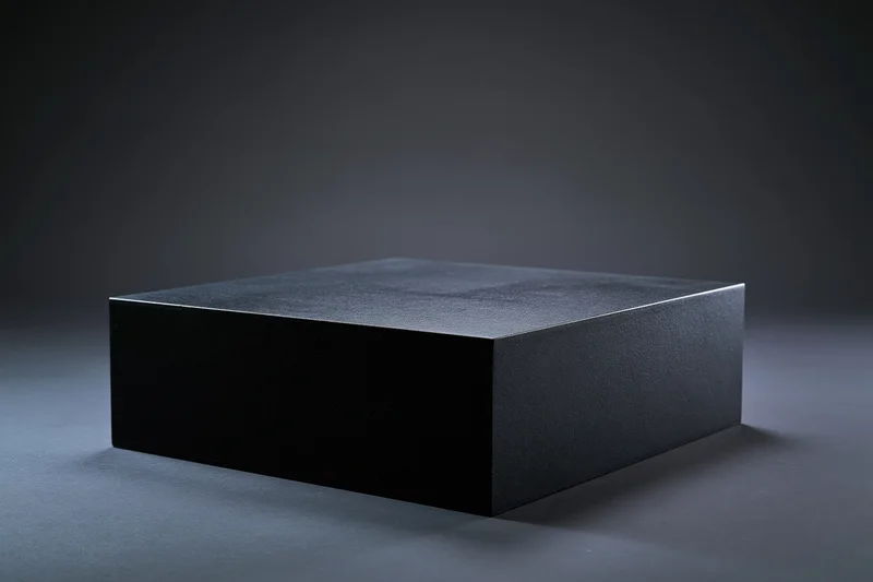 Matte black rectangular pedestal centered on dark studio floor with soft lighting and shadow