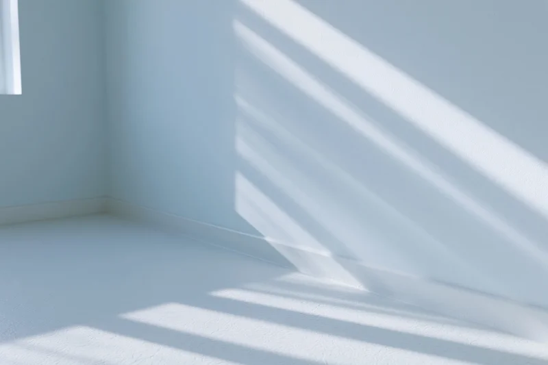 Empty minimalist room with pale blue-white walls and sunlight casting diagonal shadows across floor and wall corner