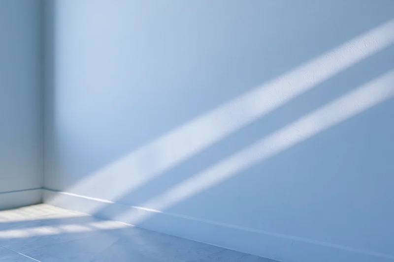 Empty minimalist room with pale blue walls and diagonal sunlight shadows on floor and corner