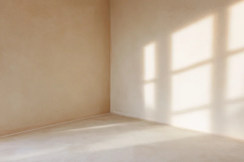 Empty minimalist room with bare beige walls and floor lit by sunlight casting window shadows in corner