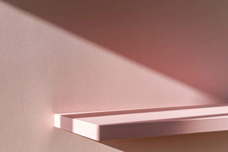 Empty blush-pink shelf mounted on a matching matte pink wall in a minimalist interior