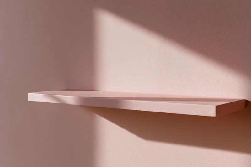 Empty pale pink wooden shelf mounted on a matching matte pink wall in a minimalist interior