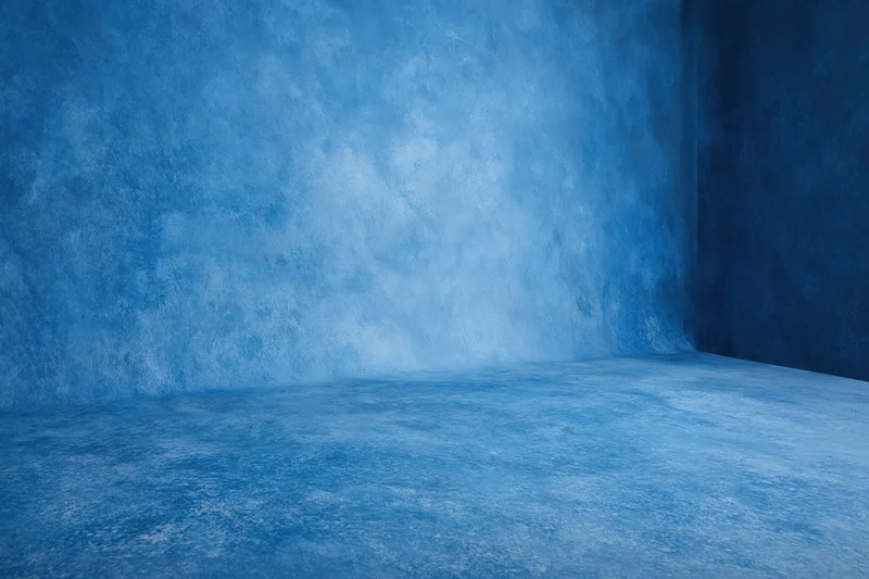 Seamless blue painted canvas backdrop in empty studio corner with textured walls and floor