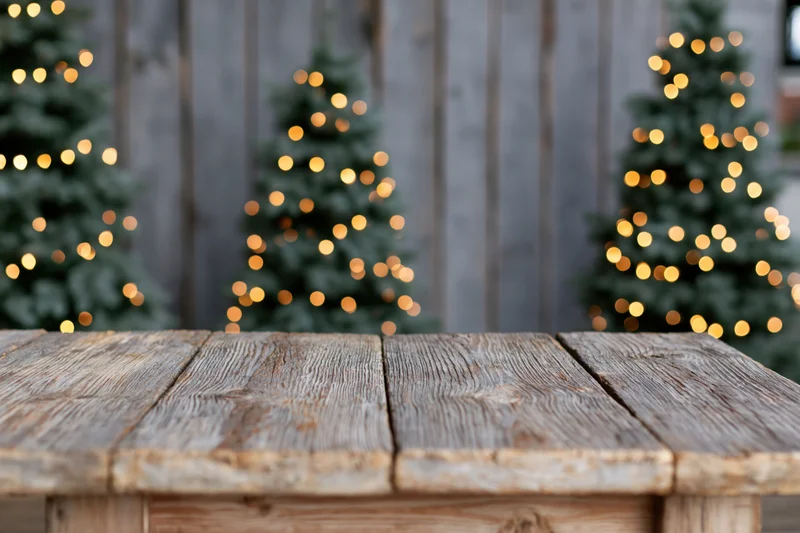 Rustic wooden tabletop in sharp focus with blurred christmas trees and lights in background