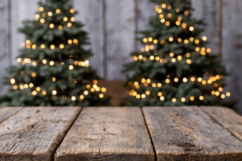 Empty rustic wooden tabletop in sharp focus with blurred christmas trees and lights in background