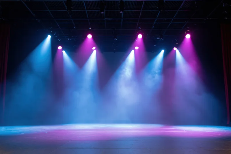 Empty theater stage illuminated by blue and pink spotlights with fog, viewed from front of house